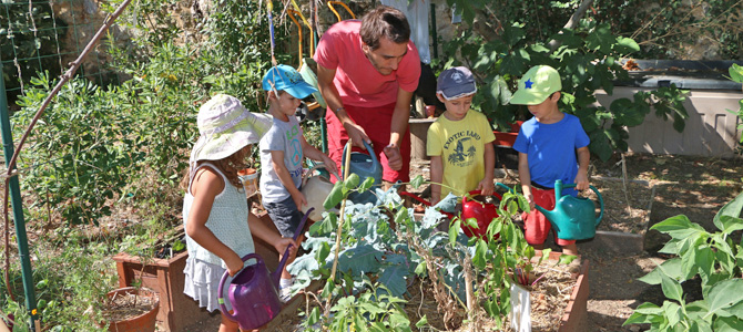 Des enfants accompagnés d'un animateur arrosent les plantations du jardin des maternels de l'Écolothèque