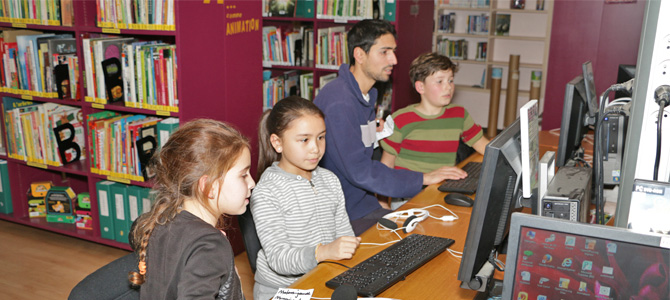 Des enfants accompagnés par un animateur effectuent des recherche internet sur les ordinateurs de la médiathèque de l'Écolothèque