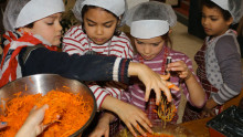 Des enfants équipés de charlottes mélangent des carottes rapées avec d'autres ingrédients pour préparer des cakes aux carottes