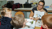 Une animatrice montre un schéma sur l'anatomie d'un oiseau à trois enfants dont un tient dans la main une image de serin cini