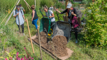 dans un jardin, des participantes déposent, avec des brouettes, une couche de terre pour élaborer une butte