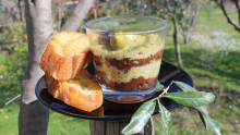 Une verrine de tapenade avec des couches noires et vertes avec deux tranches de pain grillées