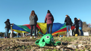 Des animateurs sont en extérieur et tiennent ensemble un grand parachute de toutes les couleurs