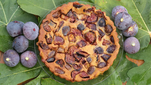 Un clafoutis est posé sur des feuilles de figuier, entouré de figues