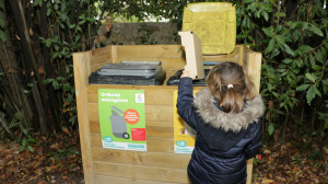 Un enfant est devant les poubelles grises et jaunes et trie du carton