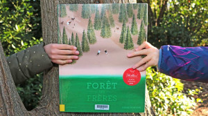 deux mains d'enfants tiennent le livre devant un tronc d'arbre