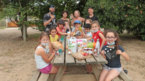 Un groupe d'enfants et leurs animateurs sont atablés et montrent le goûter qu'ils ont reçus