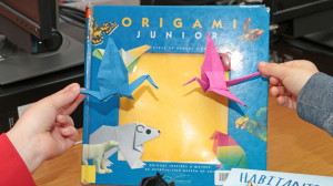 Des mains d'enfants portent des oiseaux en origami devant un livre sur l'origami