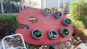 photo dans un jardin d'une grande palette de peintre contenant des pots de fleurs 