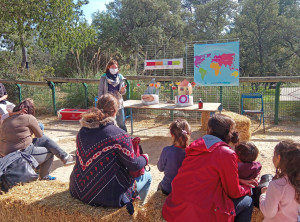 assis sur des ballots de paille, des visiteurs écoutent une animatrice au zoo